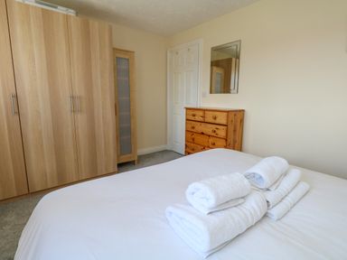 A bedroom with a bed with folded white towels on top a wooden wardrobe a wooden chest of drawers and a mirror on the wall at 74 Reap Lane Southwell near Weston