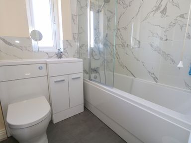 A bathroom with a toilet, sink with cabinet, bathtub with shower, and marble-patterned wall tiles at 74 Reap Lane Southwell near Weston