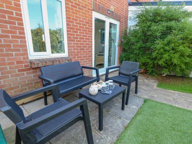An outdoor patio area with black chairs and a table set against a brick house wall at 74 Reap Lane in Southwell near Weston