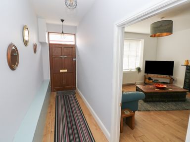 A hallway with a wooden front door and three circular mirrors on the wall leading to a living room with a television and wooden coffee table at Bryn Siriol in Narberth