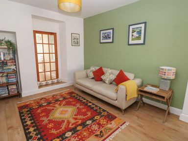 A living room with a beige sofa and colorful cushions a wooden side table with a lamp a patterned rug and bookshelves at Bryn Siriol in Narberth