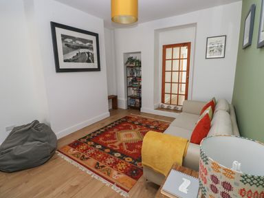 A small living room with a beige sofa, colorful cushions, a yellow blanket, a patterned rug, a bean bag, framed pictures, and a bookshelf at Bryn Siriol in Narberth