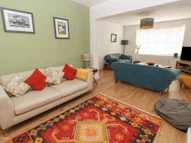A living room with a white sofa with cushions a patterned rug teal sofas coffee table and a television at Bryn Siriol in Narberth