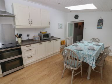 A kitchen with white cabinets a microwave an oven and a dining table set for six with blue patterned tablecloth at Bryn Siriol in Narberth