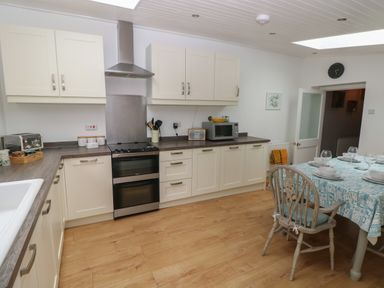 A kitchen with white cabinets wooden floor a dining table with chairs and tableware at Bryn Siriol in Narberth