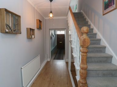 A hallway with wooden flooring, wall-mounted wooden crates, a carpeted staircase with white railing, a radiator, and a wooden front door at Bryn Siriol in Narberth