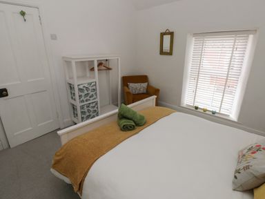 A bedroom with a bed and green towels a chair a window with blinds and a shelving unit at Bryn Siriol in Narberth