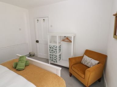 A bedroom with a white bed and green towels a mustard armchair and a white shelving unit with hangers at Bryn Siriol in Narberth
