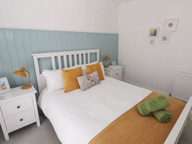A bedroom with a white bed and yellow pillows two green towels on a blanket two white nightstands with lamps and pictures on the wall at Bryn Siriol in Narberth