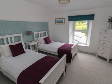 A bedroom with two single beds a nightstand a lamp a window and a chest of drawers at Bryn Siriol Narberth