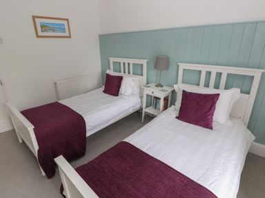 A bedroom with two single beds with purple throws and pillows a nightstand with lamp and books and a landscape painting on the wall at Bryn Siriol in Narberth