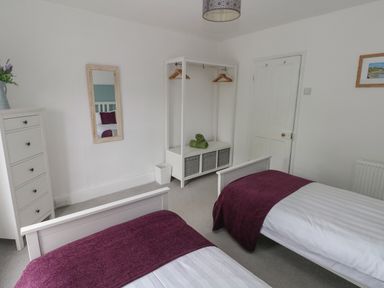 A bedroom with two single beds with purple covers a white chest of drawers a mirror an open wardrobe with hangers and towels at Bryn Siriol in Narberth