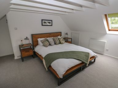 A bedroom with a bed with pillows and a green throw blanket a bedside table and a window at Bryn Siriol in Narberth