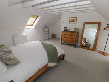A bedroom with a bed a wooden dresser a large mirror and a window on a slanted ceiling at Bryn Siriol in Narberth