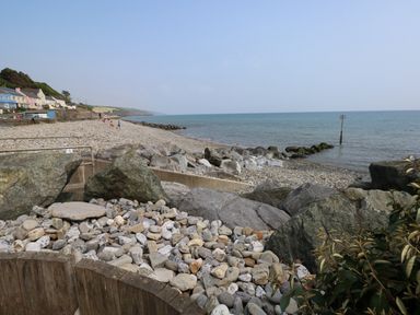 A pebble beach with large rocks and houses along the shoreline at Bryn Siriol in Narberth