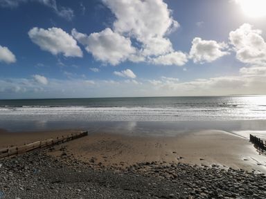 A beach with sand and pebbles and wooden groynes under a blue sky with clouds and the sea at Bryn Siriol in Narberth
