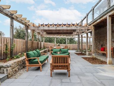 An outdoor patio with seating under a pergola at Lower Moorwood in Moorwood near Bovey Tracey