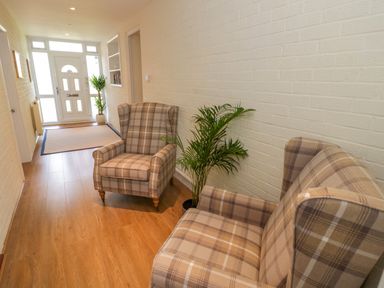 A hallway with two plaid armchairs a plant a doormat and a front door at Fenny Marina Cottage in Fenny Bentley
