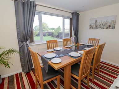 A dining room with a wooden table set with plates and glasses six wooden chairs and grey curtains at Fenny Marina Cottage in Fenny Bentley