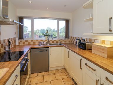 A kitchen with wooden countertops a dishwasher a toaster a kettle a bread box and a window overlooking trees at Fenny Marina Cottage in Fenny Bentley