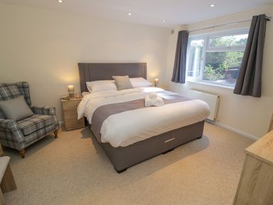 A bedroom with a bed a checked armchair bedside tables and a window at Fenny Marina Cottage in Fenny Bentley