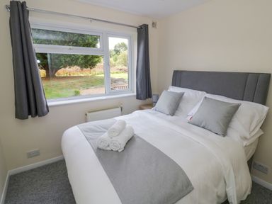 A bedroom with a bed with white and grey bedding and rolled towels on the bed near a window with grey curtains at Fenny Marina Cottage in Fenny Bentley