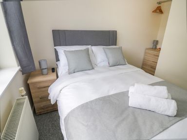 A bedroom with a bed with gray headboard and pillows bedside tables with lamps and a window with gray curtains at Fenny Marina Cottage in Fenny Bentley
