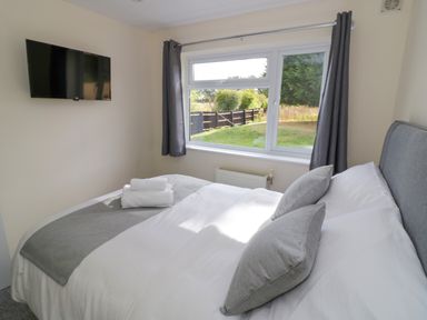 A bedroom with a bed pillows and folded towels near a window with curtains and a wall mounted television at Fenny Marina Cottage in Fenny Bentley