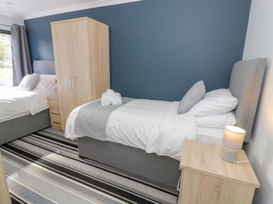 A bedroom with two single beds a wooden wardrobe a wooden bedside table with a lamp and striped carpet at Fenny Marina Cottage in Fenny Bentley