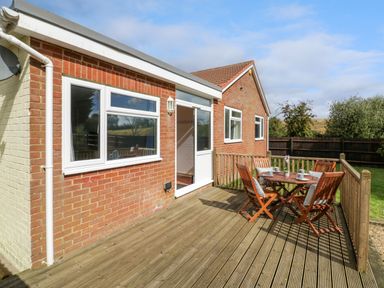A wooden deck with a table and chairs outside a brick house at Fenny Marina Cottage in Fenny Bentley