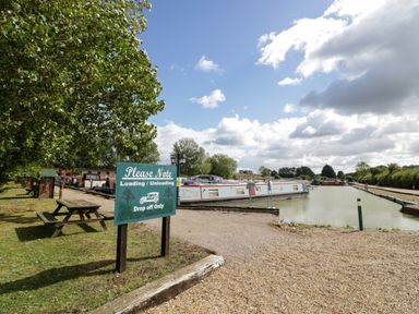 A canal with moored narrowboats and a green sign about loading and unloading near a picnic table at Fenny Marina Cottage in Fenny Bentley