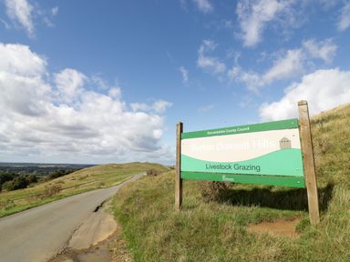 A road and grassy hills with a sign for Burton Dassett Hills by Warwickshire County Council at Burton Dassett Hills