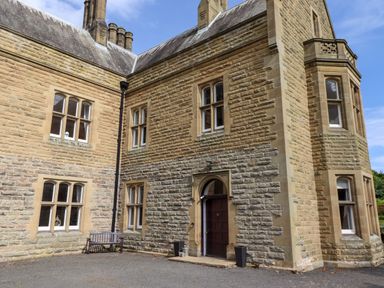 The exterior of a stone building with multiple windows a wooden bench and a dark wooden door at North Wing in Middleton Hall Estate near Belford