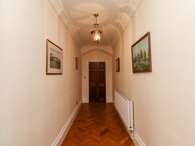 A hallway with wooden floor a radiator paintings on walls and a hanging light at North Wing Middleton Hall Estate near Belford