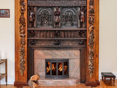 A fireplace with intricate wooden carvings and a fire burning inside at North Wing in Middleton Hall Estate near Belford