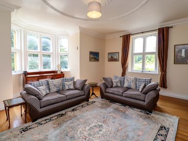 A sitting room with two sofas, a large rug, a wooden sideboard, and windows at North Wing Middleton Hall Estate near Belford