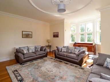 A living room with three sofas a large patterned rug wooden sideboard under bay windows and framed pictures on walls at North Wing in Middleton Hall Estate near Belford