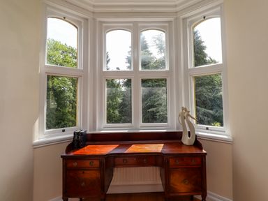 A wooden desk with books and a sculpture in front of bay windows at North Wing Middleton Hall Estate near Belford