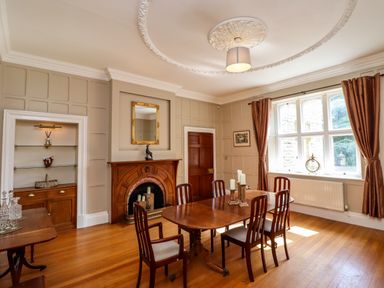 A dining room with a wooden table and six chairs a fireplace a window with curtains and a ceiling light at North Wing Middleton Hall Estate near Belford