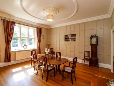 A dining room with a wooden table and chairs a grandfather clock and a window with curtains at North Wing Middleton Hall Estate near Belford