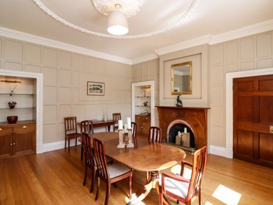 A dining room with a wooden table and chairs a fireplace with a mirror above it and built-in shelves at North Wing in Middleton Hall Estate near Belford