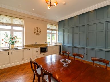A kitchen with a wooden dining table and chairs a flower vase on the counter and large built in cabinets at North Wing Middleton Hall Estate near Belford