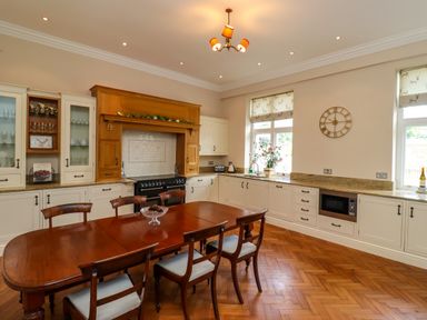 A kitchen with a wooden dining table and chairs a stove wooden cabinets countertop and windows with patterned blinds at North Wing in Middleton Hall Estate near Belford