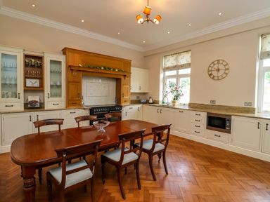 A kitchen with a wooden dining table and six chairs white cabinets wooden flooring and a large stove at North Wing Middleton Hall Estate near Belford