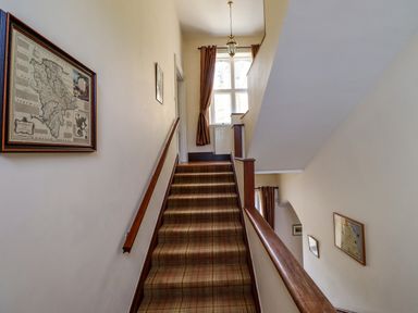 A staircase with carpet and wooden handrails with framed maps on the walls at North Wing in Middleton Hall Estate near Belford
