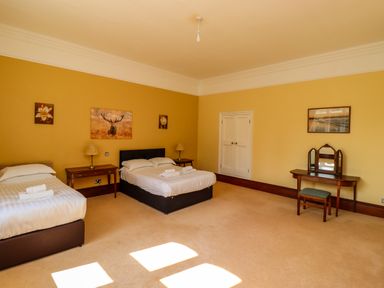 A bedroom with two beds a dressing table and three paintings on yellow walls at North Wing Middleton Hall Estate near Belford