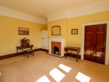 A room with a fireplace a mirror above it a small wooden table a dressing table with a mirror and a stool and wooden double doors at North Wing Middleton Hall Estate near Belford