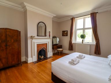 A bedroom with a bed towels on it a wooden wardrobe a fireplace a dressing table with a mirror and window with curtains at North Wing Middleton Hall Estate near Belford