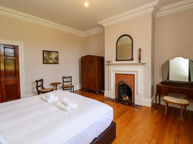 A bedroom with a bed, fireplace, wooden chairs, wardrobe, and dressing table at North Wing in Middleton Hall Estate near Belford