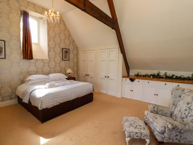 A bedroom with a double bed two framed pictures a floral armchair and ottoman and built-in cabinets at North Wing in Middleton Hall Estate near Belford